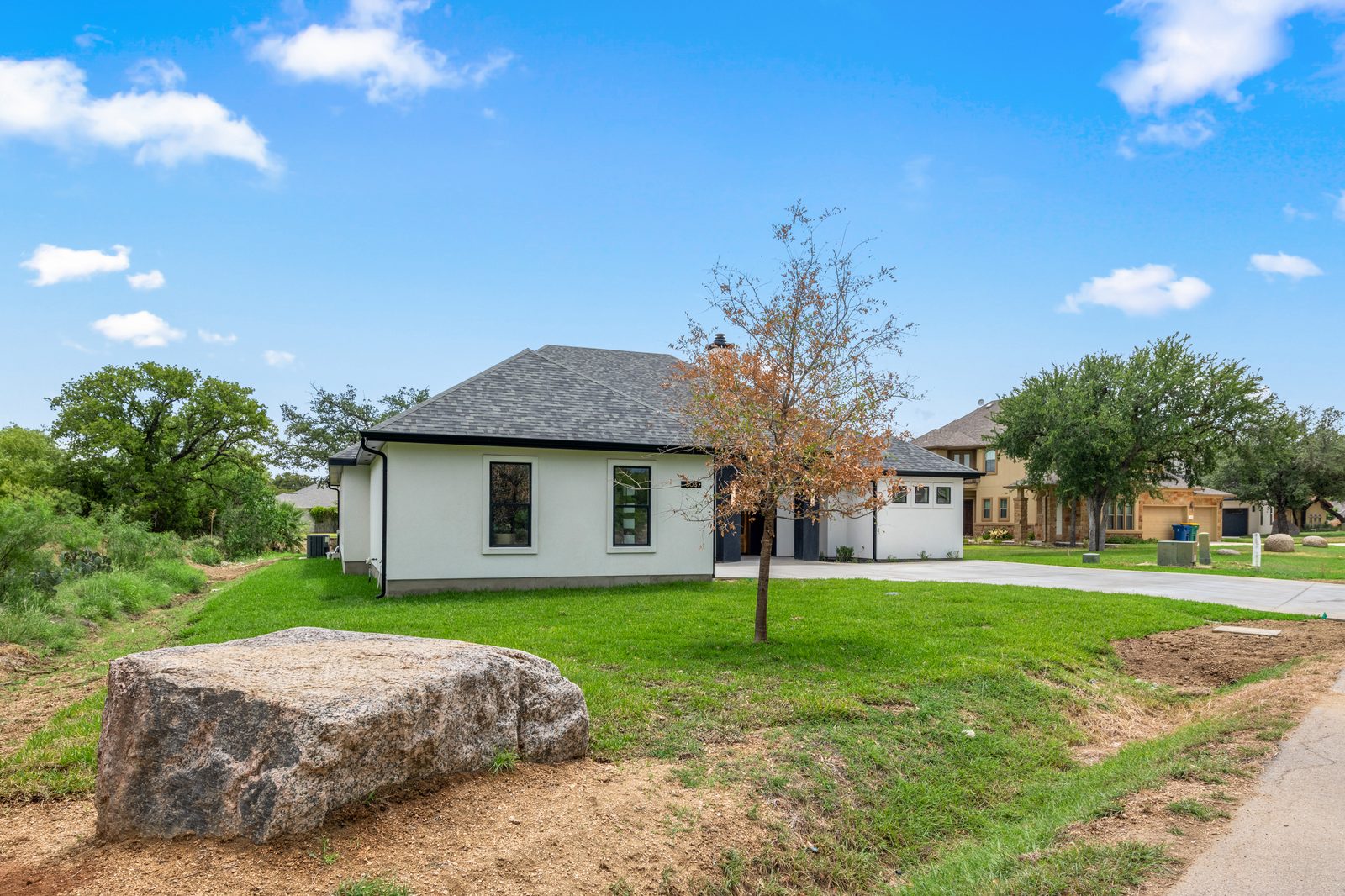 Exterior of 308 Belaire Drive with limestone boulder and young Texas oak