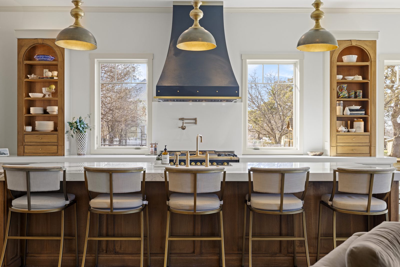 409 E Main kitchen with brass pendants, deep-blue range hood, and arched display cabinets