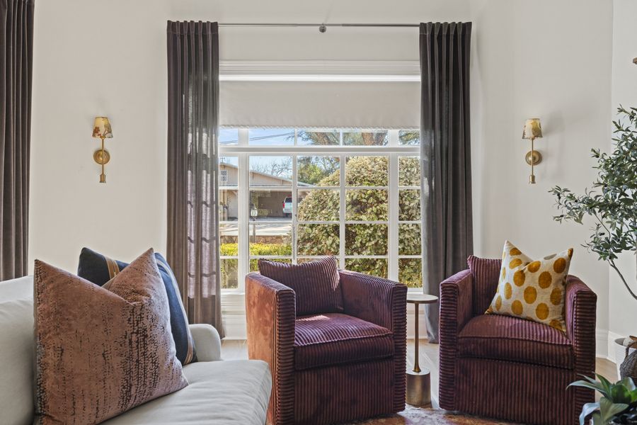 Formal sitting room with two plum corduroy chairs, brass sconces, and pinch-pleat drapery