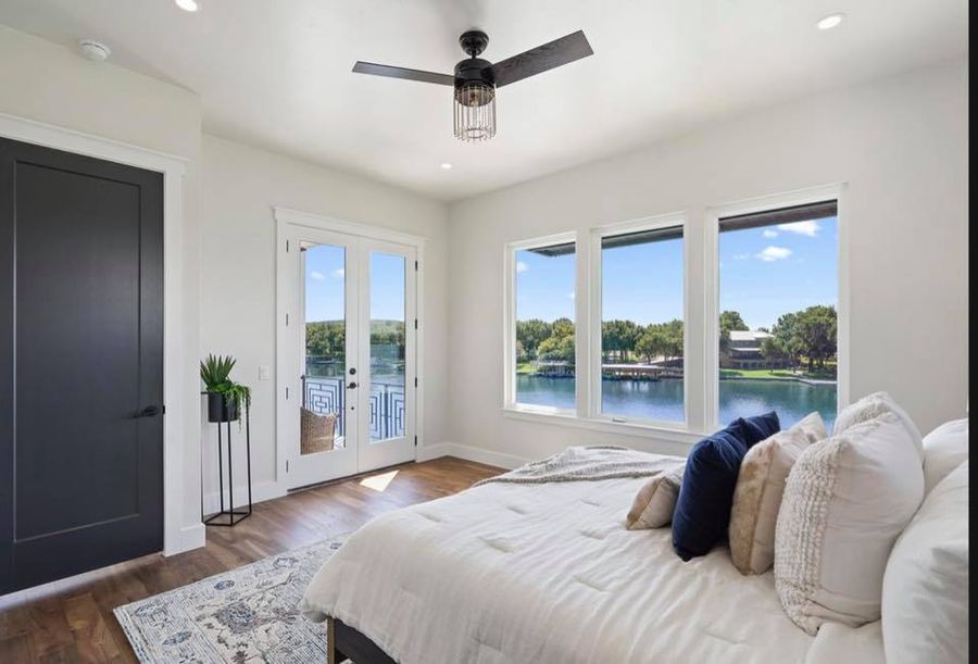 Master bedroom looking out onto Lake LBJ, with soft cream linens and a dark hand-rubbed door