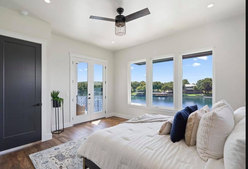 Master bedroom with Lake LBJ views through three large windows, soft cream linens and dark door accents